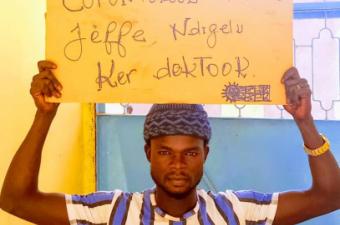 Bamba Badiane, Migrants as Messengers volunteer in Senegal, holds up a handwritten message as part of a Covid-19 myth-busting photo campaign. The words, in Wolof, translate as: “Garlic does not cure [coronavirus], let's respect sanitary measures”. 
